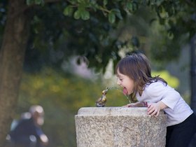 Mädchen trinkt aus einem Brunnen